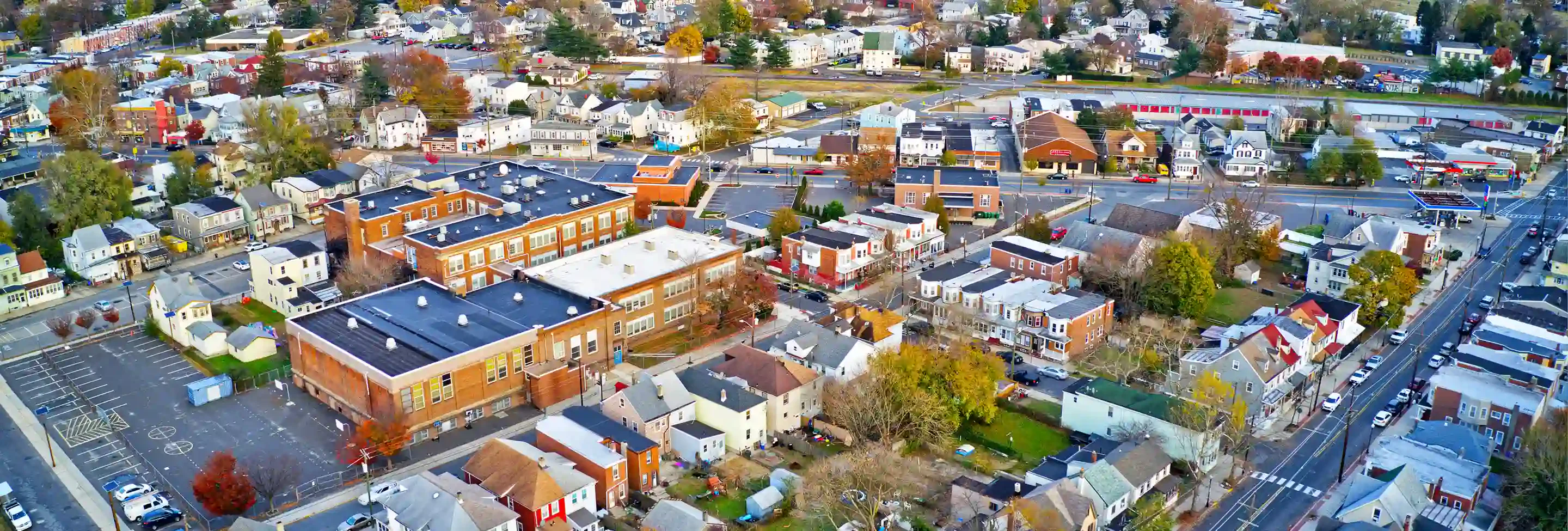 Aerial view of a small town showcasing residential areas, schools, and streets lined with colorful houses and trees in autumn foliage.
