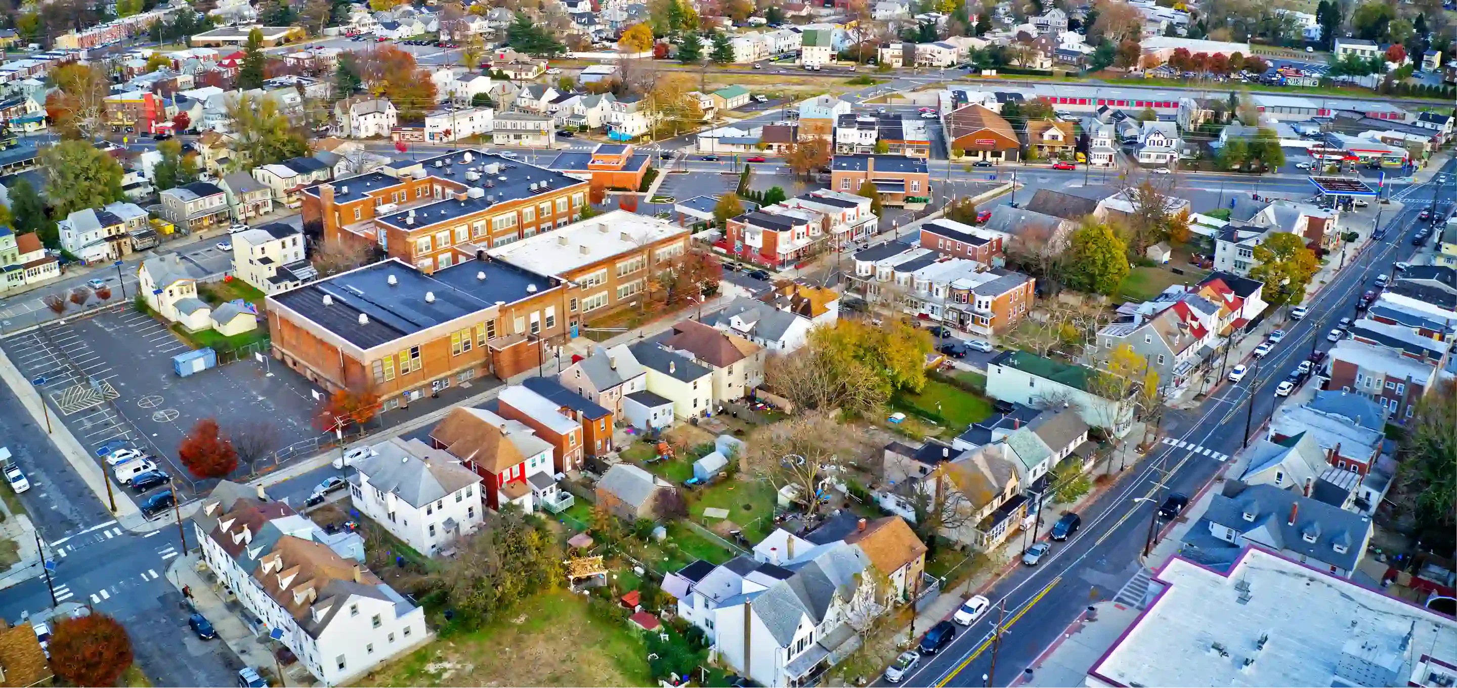Aerial view of a small town showcasing residential areas, schools, and streets lined with colorful houses and trees in autumn foliage.