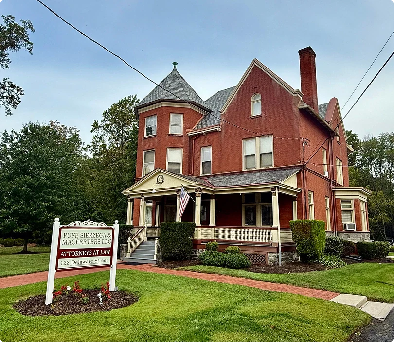 Historic red brick law office with an American flag, surrounded by lush greenery and autumn flowers, under a clear blue sky.